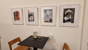 Vernissage Farbe, Form & Fantasie Bernd Wilms Vier gerahmte Collagen an einer weißen Wand mit Stehtisch im Vordergrund