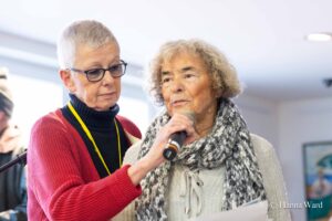 Inke Asmussen hält das Mikrofon für eine ältere Teilnehmerin der Ausstellung, die ein Gedicht vorträgt