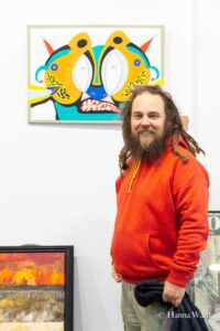 Ein Künstler im orangen hoody vor seinem Bild