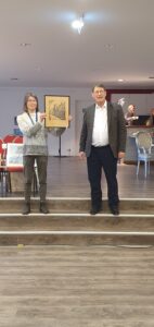 Die Organisatorin und der Auktionator bei der bieten einen Holzschnitt zum Kauf an.