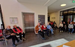 Gäste und die Künstlerin im Foyer des Quartier 36 bei der Eröffunungsrede. Alle sitzen.