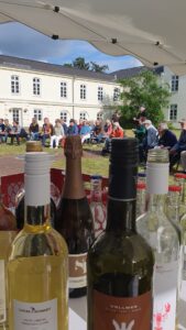Wein und Sektflaschen im Vordergrund, dahinter Besucher der Veranstalung sitzend.