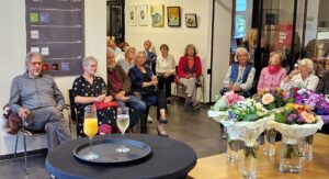 Gäste der Veranstaltung. Im Vordergrund 5 Blumensträuße auf einem Buchentisch.