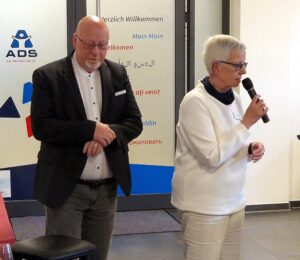 Inke Asmussen am Mikrofon, neben ihr ein Ratsherr der Stadt Schlewig. Er trägt ein schwarzes Sakko.