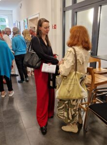 Andrea Stephan in roter Hose und schwarzer Bluse im Gespräch mit einer Besucherin.