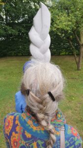 Nordart 2025 Foto: Meike Roos Frau mit Zopf von hinten vor einer Skulptur mit Zopf.