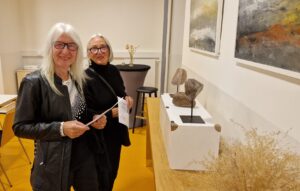 Zwei Frauen, in schwarz gekleidet, vor Monotypien und Skulpturen.