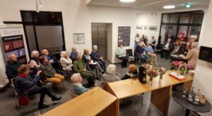 Blick von der Treppe im Foyer des Quartier 36 auf die Vernissage. Der Raum ist gut mit Gästen befüllt.