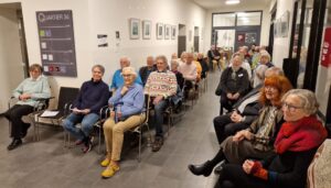 Blick in das Foyer des Quartier 36, das die Gäste der Vernissage zeigt. Alle sitzend und den Blick nach vorn.