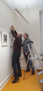 Zwei Männer hängen Bilder auf.