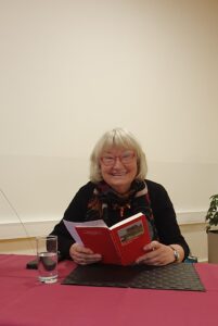 Annegret Vahle mit Buch am Tisch sitzend lächelt in die Kamera.