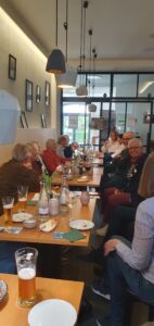 Teilnehmende der Veranstaltung an einem langen Tisch. Es stehen Schnacks und Getränke auf dem Tisch.