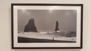 Schwarz-weiß Foto eines Strandes mit aufgewühlter See und zwei bizarren Felsen im Hintergrund und eines Kindes, das über den Strand läuft im Vordergrund.