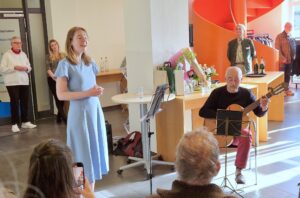 Die Sängerin Kristjana Dreier singt. Sie trägt ein hellblaues Kleid. Sitzend an der Gitarre Martin Jung.