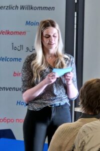 Anna Greil hält eine Laudatio. Sie hat blonde lange Haare und ist dunkel gekleidet.